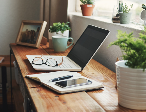 A laptop, notebook, and mobile phone on top of a home desk